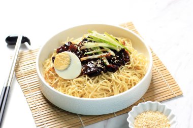 Jajang Myeon ya da JJajangmyeon Kore Noddle yanında salatalık ve susam tohumu ile servis edilir.