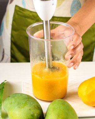 El blenderi kullanan bir kadın mango suyu (meyve suyu) yapıyor. Mango veya Mangga Tropikal Meyve Favorisi
