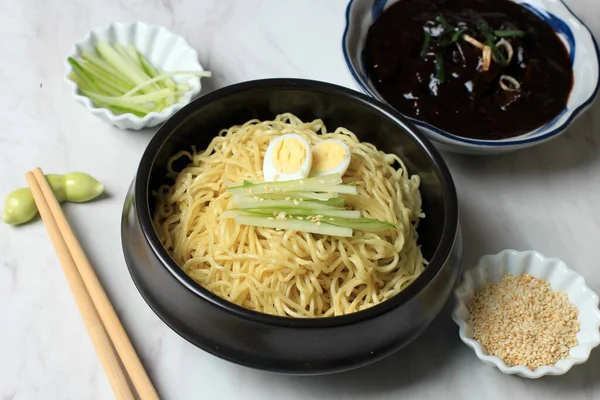 Jajangmyeon ya da JJajangmyeon Kore Noddle yanında salatalık ve susam tohumu ile servis edilir.