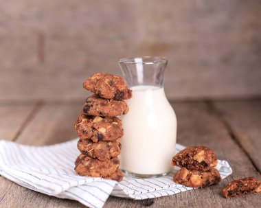 Stacked Homemade Chocolate Chips Cookies with Macadamia Nut, Served with a Bottle of Milk. Copy Space for Text, Recipe or Advertisement on Wooden Rustic Background. Selective Focus