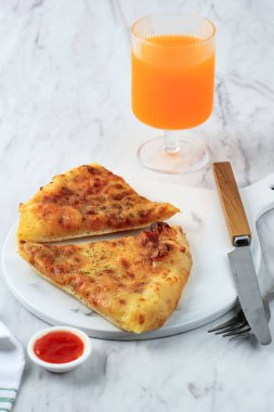 İki dilim peynirli pizza ve bir bardak portakal suyu, beyaz masada.