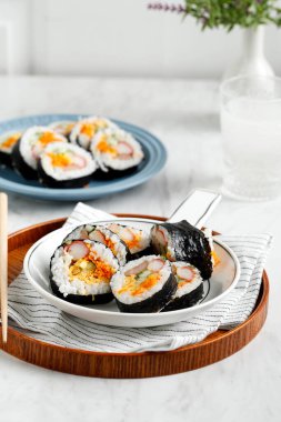 Kyuri, Havuç, Sosis, Yengeç Çubuğu veya Kimchi gibi çeşitli malzemelerden yapılan Kimbap (Kimbob veya Kimbap) ve buğulanmış Beyaz Pirinç (Bap) karışımından yapılmıştır..