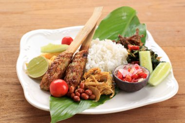 Nasi Kampüsü Bali. Çeşitli Tabaklar ve Birlikte Hizmet Verilen Popüler Bale Pirinç Yemeği. Bu menü Ayam Sisit, Sate Lilit, Saute Papaya Leaf ve Sambal Matah içerir..