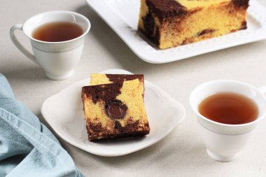 Lezzetli ev yapımı dilimlenmiş kremalı arka planda yarım kiloluk kek, çay ile servis edilir.