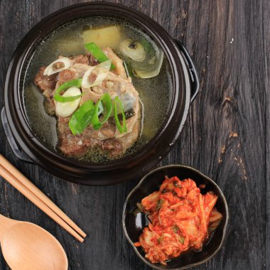 Top View Sop Buntut Gori Gomtang (Sokkori Gomtang) veya Kore Oxtail Çorbası, Kimchi ve Dilimlenmiş Yeşil Soğan ile birlikte Kara Kore Bowl 'unda servis edilir.