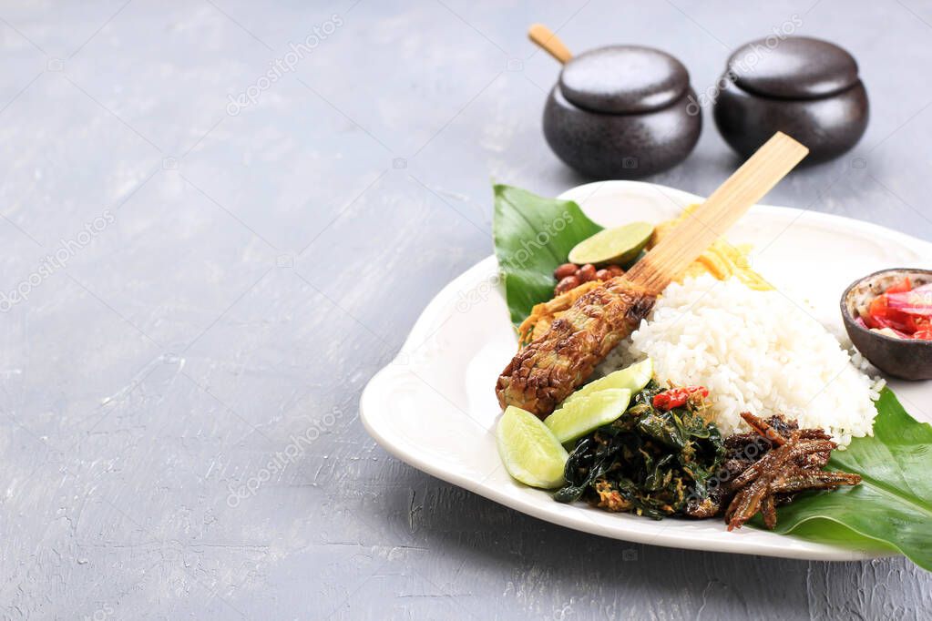 Nasi Campur Bali. Popular Balinese Meal of Rice with Various Side Dish, Served Together. This Menu Contains Ayam Sisit, Sate Lilit, Saute Papaya Leaf, and Sambal Matah. Copy Space for Text