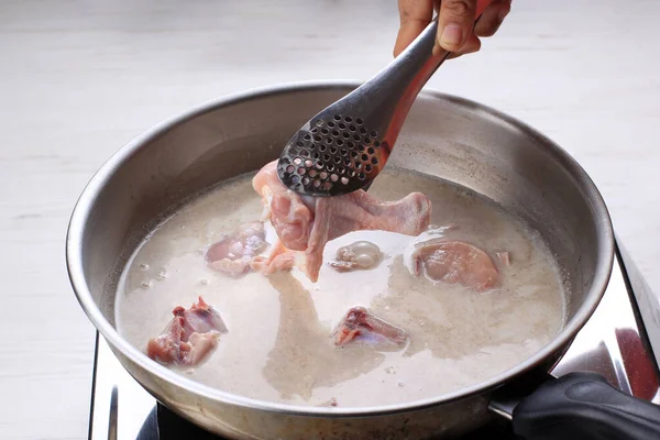 Indonesian Home Cooking Process, Female Hand Add Chicken Thigh Drumstick to the Pan using Tongs, Making Indonesian or Thai Style Curry, Traditional Asian Gourmet Called Opor Ayam, Gulai, Kari, or Kare