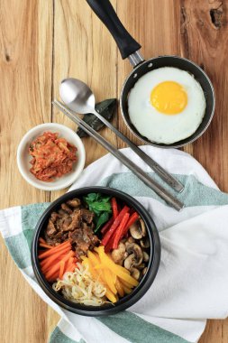 Korean Bibimbap, Nixed Rice with Vegetable, Rice, and Egg. Served with Kimchi. Top View on Wooden Table