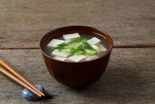 Japanese Miso Soup with Spring Onion and Cubed Tofu Cheese, In a Brown Bowl, Wooden Table. Copy Space for Text