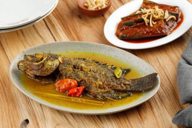 Spicy Gourami Fish Stew in Yellow Curry Spice. Thai and Indonesia Style Food. On Wooden Table 