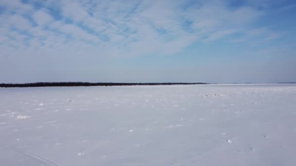 ドローン撮影 雪の中で凍った川を飛んでいる 氷は雪の下にあり 他の海岸は遠くに見えます — ストック動画