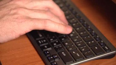 Bir adamın eli klavyede yazı yazıyor. Odada akşam aydınlatması var. Kısa odaklı yakın plan bir statik plan. 