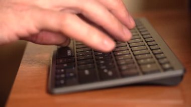 Bir adamın eli klavyede yazı yazıyor. Odada akşam aydınlatması var. Kısa odaklı yakın plan bir statik plan. 