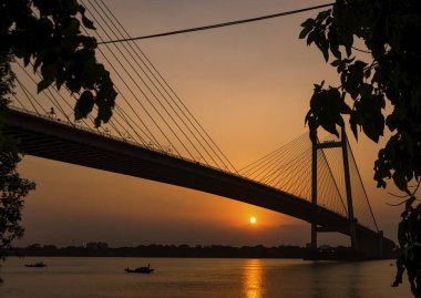 Akşam saatlerinde Vidyasagar Setu, Kolkata 'nın silueti. Ganj nehrinden geçen tekneyle güneş batıyor. Seçici odak.