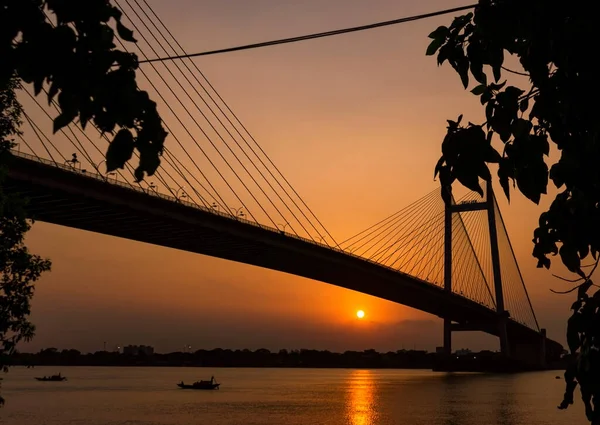 Akşam saatlerinde Vidyasagar Setu, Kolkata 'nın silueti. Ganj nehrinden geçen tekneyle güneş batıyor. Seçici odak.