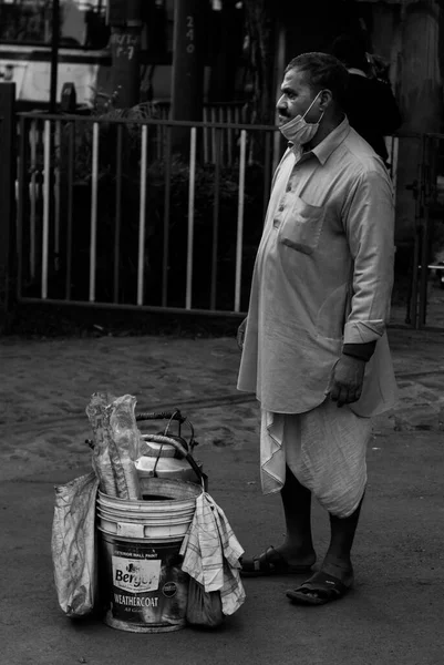 インドのコルカタ 2022年1月2日 伝統的なインドの道祖神を身に着けているお茶の販売店 立って顧客を待っています 茶釜と紙コップが入ったバケツが前に置かれている モノクローム 選択的焦点 — ストック写真