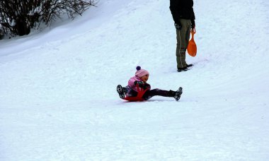 Dnepropetrovsk, Ukrayna - 12.31.2021: Küçük kız ve baba kışın kızaktan kayarak kayıyorlar. Çocuklar için açık hava oyunu.