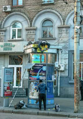 Dnipropetrovsk, Ukrayna - 11.26.2021: Bir büfenin çatısında çalışan bir işçi elektrikli matkapla ışıklandırma cihazları kuruyor. İşçi büfenin çatısında yatıyor..