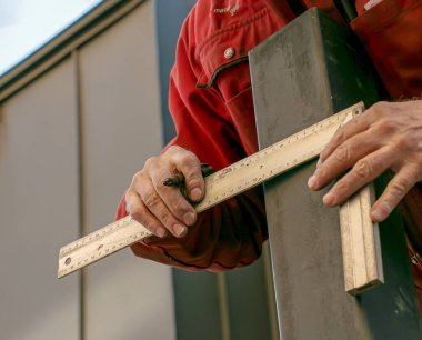 Yetenekli bir işçi ölçer ve demir cetvelle kare bir borunun üzerinde bir çizgi çizer..