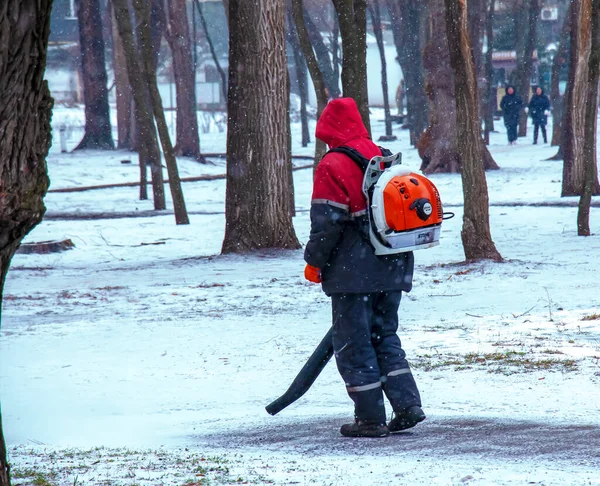 Dnepropetrovsk, Ukrayna - 02.04.2022: Parktaki kamu hizmetlerinin mevsimsel çalışmaları. Motorlu sırt çantalı bir işçi park yolundan kar üflüyor..