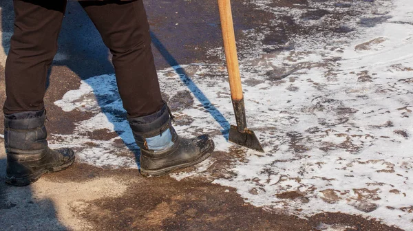 A woman worker cleans the ice and removes snow from paving slabs using an icebreaker. A man breaks ice with a steel blade crusher, an ice-breaking tool. The janitor cleans up the area.