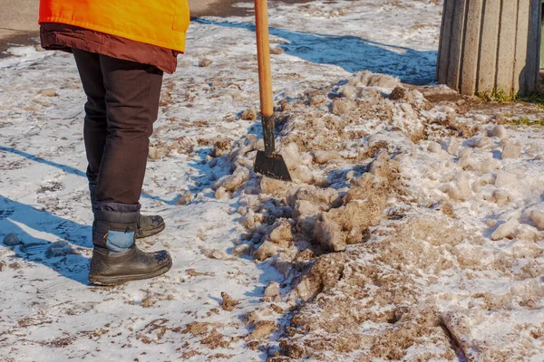 A woman worker cleans the ice and removes snow from paving slabs using an icebreaker. A man breaks ice with a steel blade crusher, an ice-breaking tool. The janitor cleans up the area.