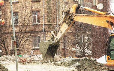Dnepropetrovsk, Ukrayna - 02.04.2022: Kazıcı karlı havada çalışır. Kazı kovası kazılan toprağı hareket ettirir..