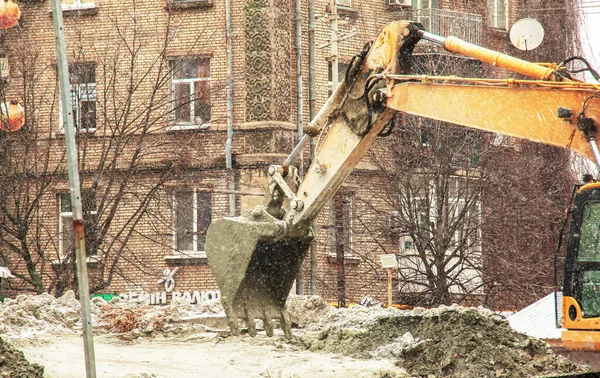 Dnepropetrovsk, Ukrayna - 02.04.2022: Kazıcı karlı havada çalışır. Kazı kovası kazılan toprağı hareket ettirir..