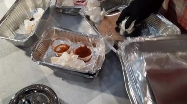 Yaşlı bir kadın yemekten sonra masayı temizler. Siyah eldivenli eller öğle yemeğinden kalan kutuları istifledi. Paketler geri dönüşüm için ayrı çöp kutularına konuyor..
