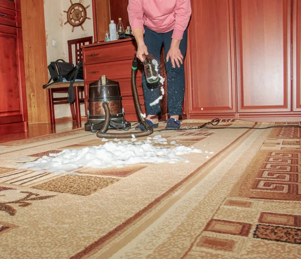 Halıyı su filtresiyle elektrikli süpürgeyle temizleme işlemi. Bir kadın kirli halı yüzeyine temizlik köpüğü sürer..