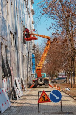 Dnepropetrovsk, Ukrayna - 02.09.2022: Bir vinç sepetinde inşaatçı binanın ön cephesindeki metal bir yapının kaplamasını onarıyor.