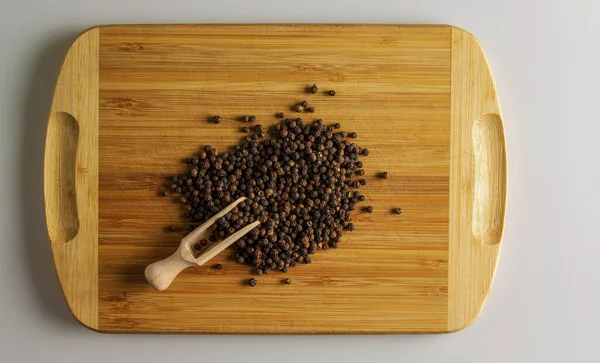 Black peppercorns. Aromatic spice for food. Background of dried black pepper seeds on a wooden kitchen board with a measuring spoon.