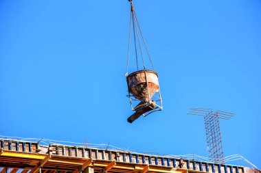 Bir vinç, konut binasının modern metal beton yapısı için beton kaldırır. Mavi gökyüzüne karşı beton kaplı konteynır.