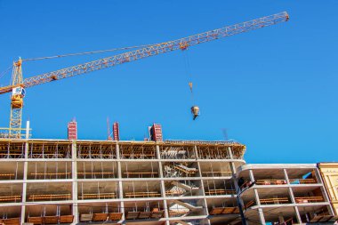 Bir vinç, konut binasının modern metal beton yapısı için beton kaldırır. Mavi gökyüzüne karşı beton kaplı konteynır.