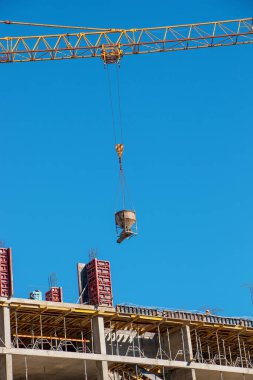 Bir vinç, konut binasının modern metal beton yapısı için beton kaldırır. Mavi gökyüzüne karşı beton kaplı konteynır.
