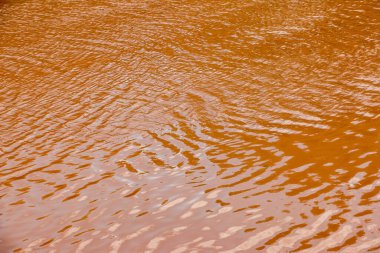 Nehrin su yüzeyi turuncudur. Açık kahverengi nehir arka planı. Sudaki ipeksi kil bileşikleri.