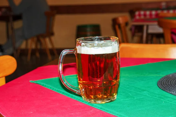 Close-up of a glass of fresh foamy beer on a table covered with a red-green tablecloth.