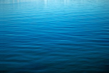 Water ripple texture. Blue background of the water surface. Wavy water surface during the day in bright sunlight.