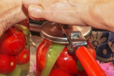 The process of preserving tomatoes for the winter. Women's hands close the lids of jars with ripe red juicy tomatoes with a special key.