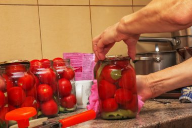 The process of preserving tomatoes for the winter. Women's hands close the lids of jars with ripe red juicy tomatoes with a special key.