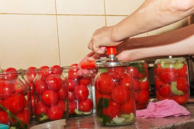 The process of preserving tomatoes for the winter. Women's hands close the lids of jars with ripe red juicy tomatoes with a special key.