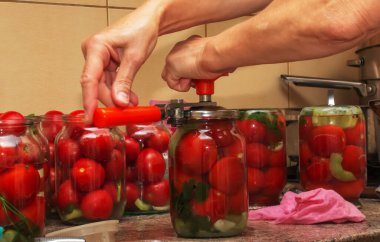 The process of preserving tomatoes for the winter. Women's hands close the lids of jars with ripe red juicy tomatoes with a special key.