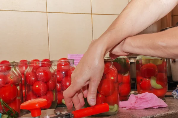 The process of preserving tomatoes for the winter. Women's hands close the lids of jars with ripe red juicy tomatoes with a special key.