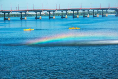 Athletes in kayaks in training near the river fountain in a rainbow of splashes.