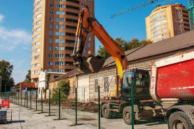 Kazı işe yarıyor. Traktörün kovası toprağı inşaat alanındaki bir çöp kamyonunun arkasına kürekle dolduruyor..