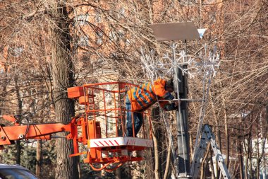 Dnipro, Ukrayna - 02.15.2022: Gezici hava platformunda turuncu üniformalı belediye servis çalışanları yeni yılın elektrik çelenklerini onarıyorlar.