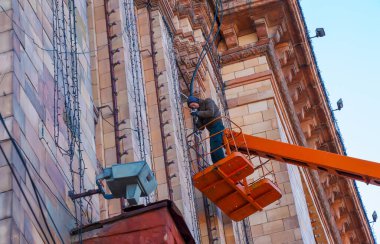 Dnipro, Ukrayna - 02.15.2022: Gezici hava platformunda turuncu üniformalı belediye servis çalışanları yeni yılın elektrik çelenklerini onarıyorlar.