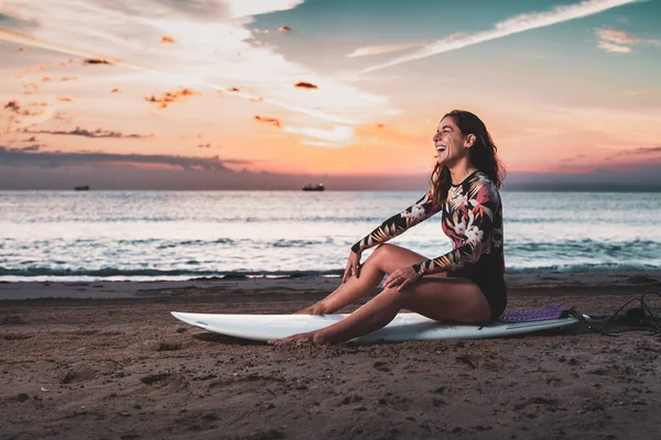 Woman sitting on surfboard on sand on beach at dawn