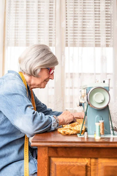 profile portrait of an older woman with white hair focused on her work in front of a sewing machine. horizontal