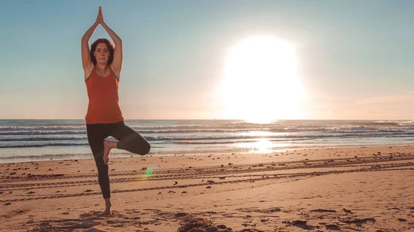 woman in yoga pose on the beach with the sun rising from the ocean. horizontal